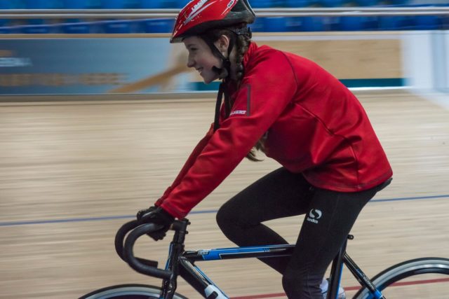 A female pupil riding a bike in the school sports kit.