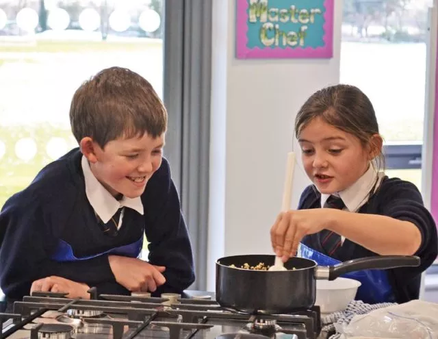 A boy and girl cook together whilst looking at a saucepan