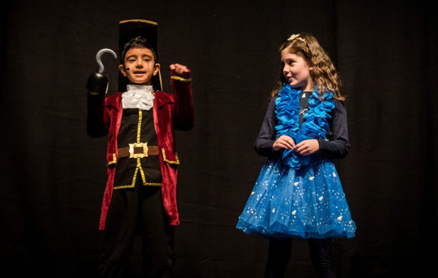 Two young children stood together on the stage in drama production