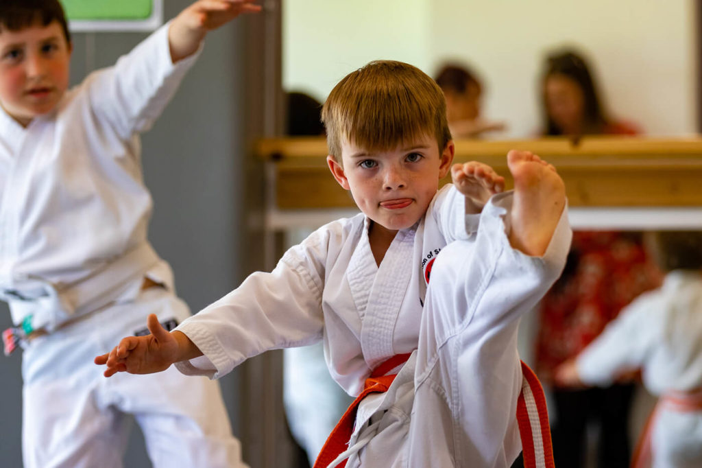 Primary school boy wearing a judo suit and performing a high leg kick