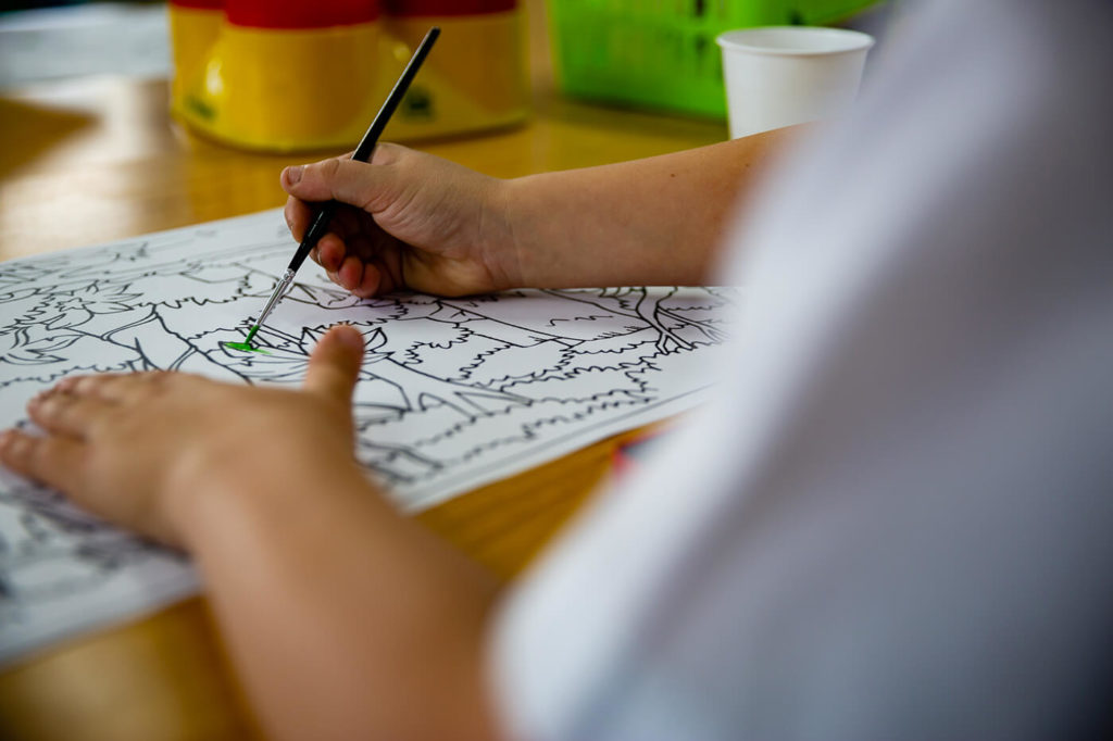 Young hands holding a paint brush, painting an activity sheet