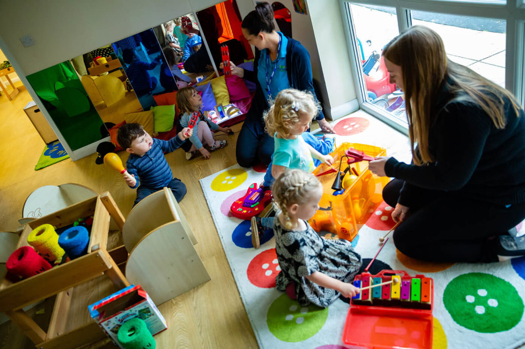 Nursery assistants supervise a group of small children playing with toys in The Elms nursery.