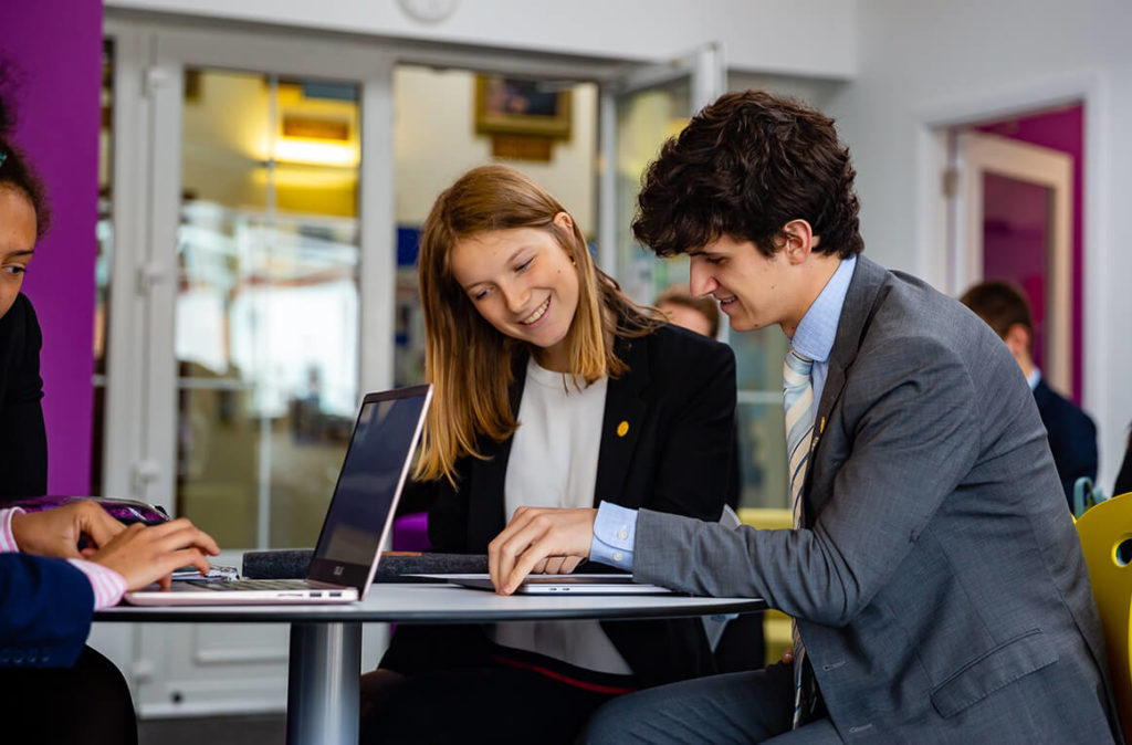 Teenage girl and boy sat at a table together looking at a report