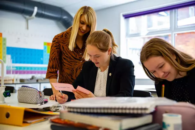 A chemistry teacher supporting two Sixth Form pupils in the classroom