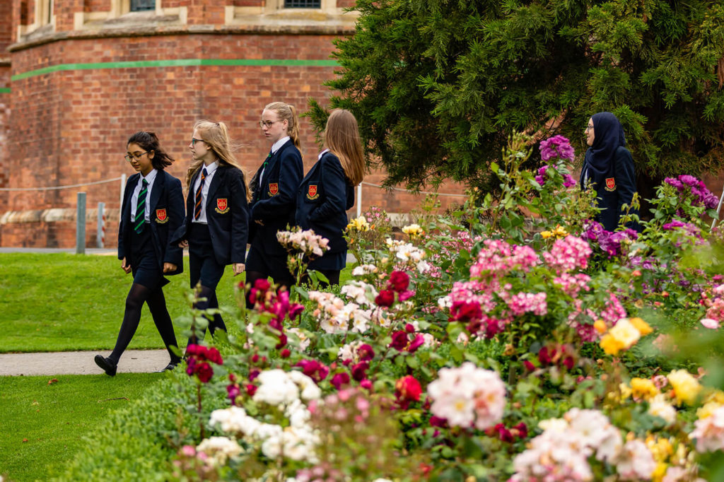 Three female pupils walk through the Trent College grounds near beautiful flowers