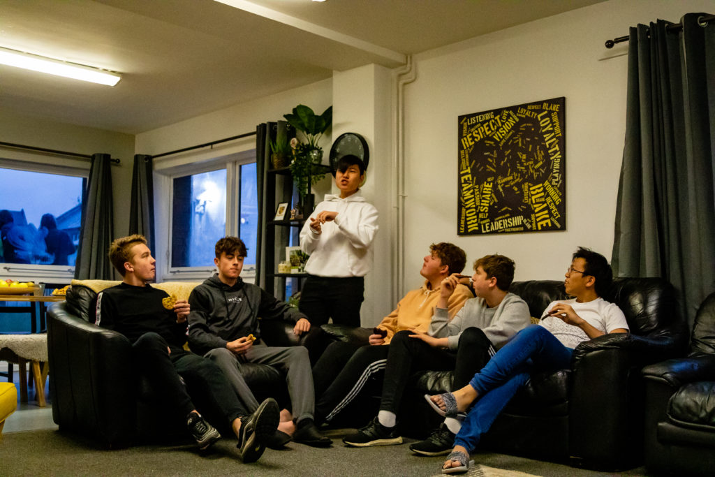 six teenage boys sitting in a shared living room space