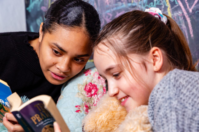 Two Year 7 boarders smile whilst reading a book with a teddy bear