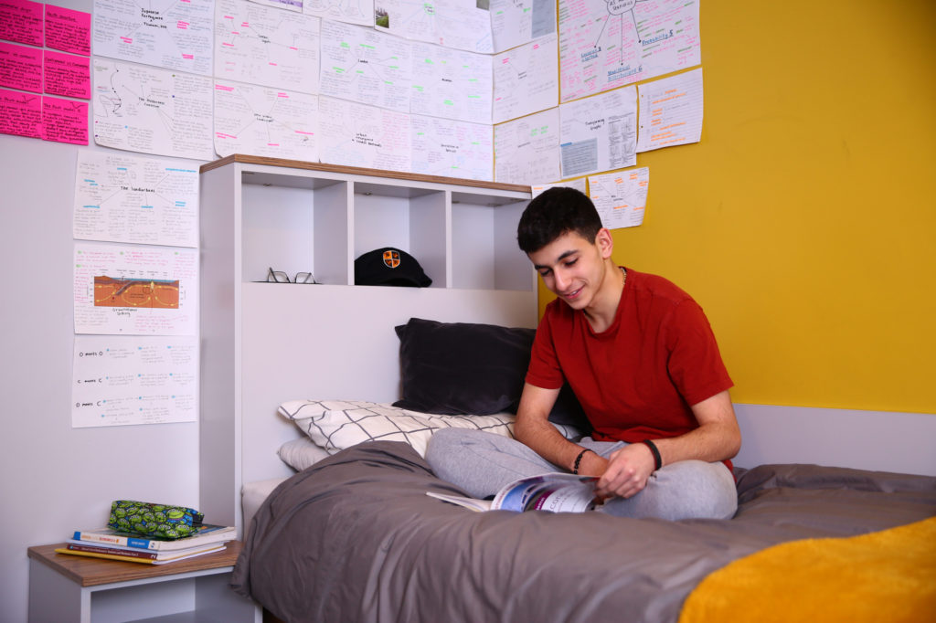 sixth form boy sat on a bed in a bedroom