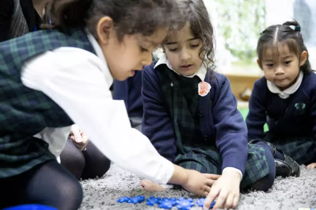 Two primary school children sat on the floor together playing with counters