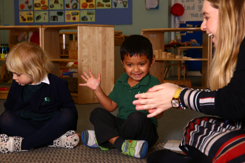 Pre-school child sat with a teacher clapping