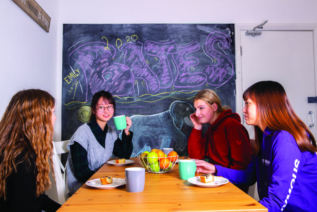 Sixth form girls sat at table chatting and drinking tea and coffee