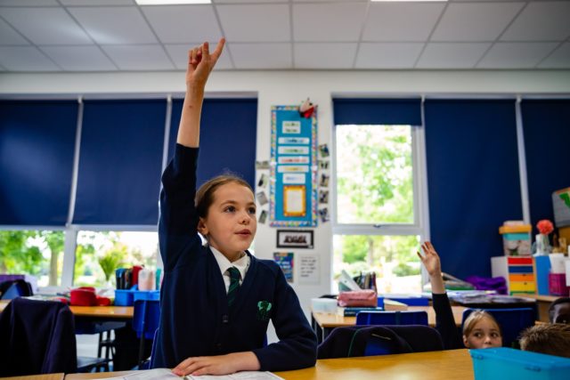 Young school girl sat with hand raised in a classroom