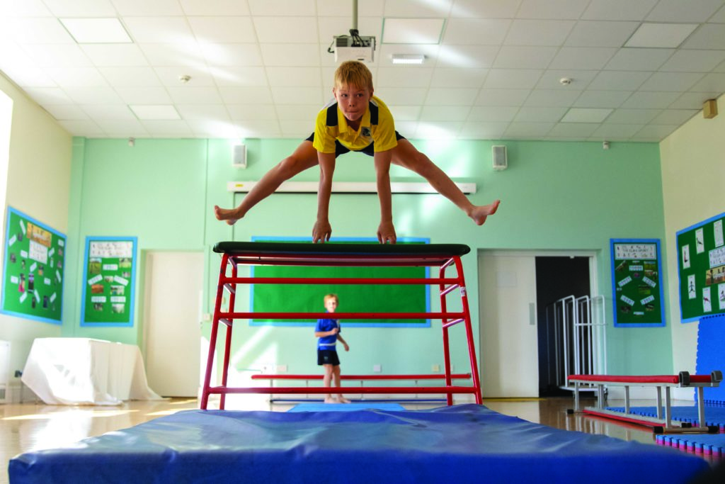 Young boy straddle jumping over gym apparatus